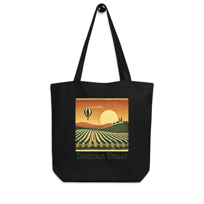 Black tote bag with a vintage-style illustration of Temecula Valley vineyards, a setting sun, and a hot air balloon floating above the landscape.