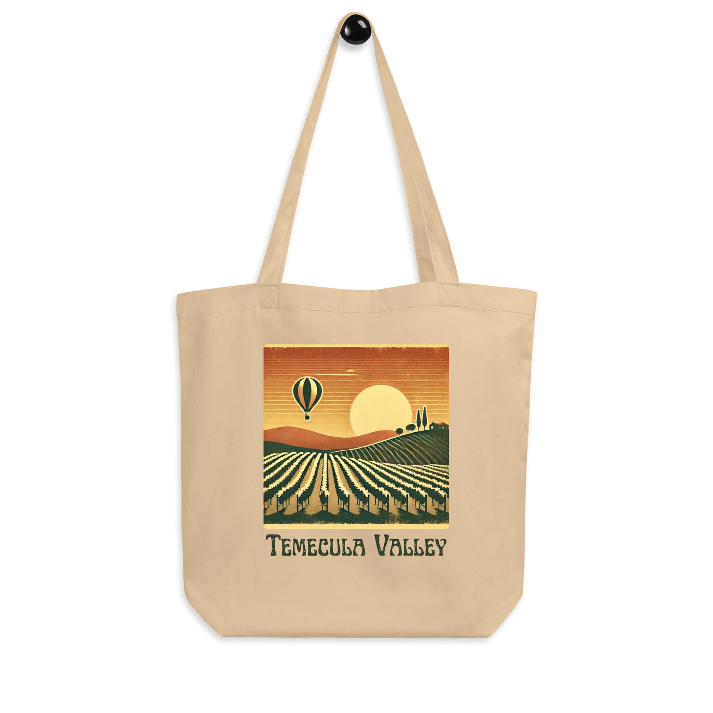 Beige tote bag with a vintage-style illustration of Temecula Valley vineyards, a setting sun, and a hot air balloon floating above the landscape.